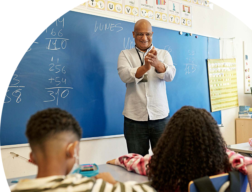 Teacher standing in front of a blackboard teaching students.